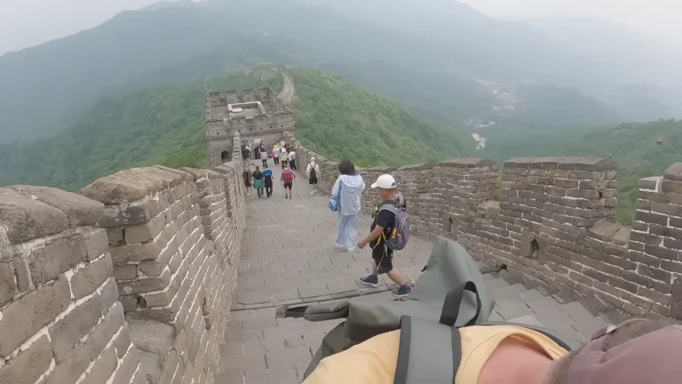Visitors walking along an ancient stone wall over green hills in China