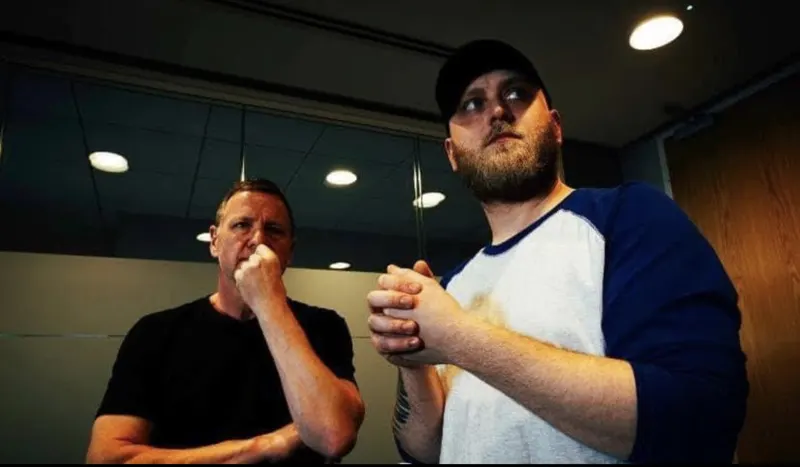 Andy Blithe directing on set, hand to chin beside a bearded actor