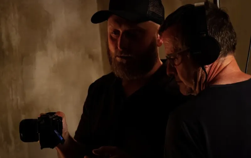Andy Blithe on set in headphones, checking a camera with a bearded crew member