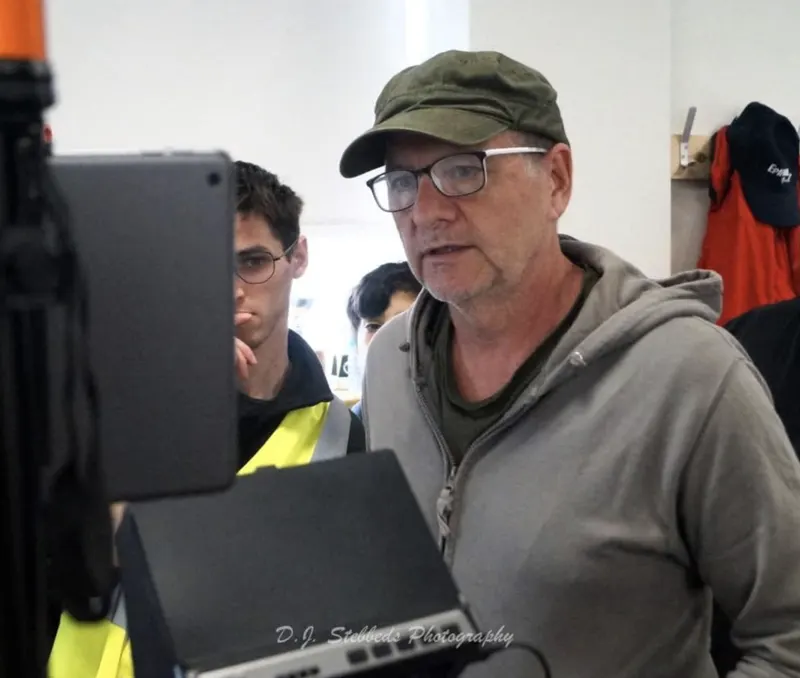 Andy Blithe directing on set, checking the monitor in a green cap