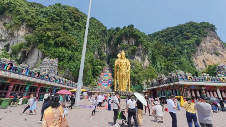 Colourful temple steps and a golden statue below limestone cliffs in Malaysia