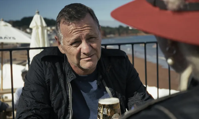 Andy Blithe film still, at a seaside pub table with a pint
